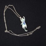 В таинственных землях Эльдариона, где магия сплетается с реальностью, был создан этот волшебный кулон в виде игривого кота. Словно сотканный из лунного света и осколков звёздного неба, он покоится на изящной серебряной цепочке, которая переливается, будто сотканная из нитей древней магии. Кот на подвеске — не просто украшение, а хранитель маленьких секретов. Его полупрозрачная фигура, созданная из эпоксидной смолы, словно застыла в прыжке, а на шерсти мерцает узор, напоминающий лепестки зачарованного цветка. Говорят, что этот узор способен менять оттенки в зависимости от настроения владельца: становится нежно-голубым, когда сердце наполнено радостью, или глубоким фиолетовым, если душа тоскует. Легенда гласит, что этот кот — дух-хранитель, призванный оберегать своего владельца от бед и невзгод. В полнолуние он оживает на мгновение, чтобы прошептать на ухо своему хозяину древние истины или предупредить о грядущей опасности. Его хвост — это нить судьбы, связывающая владельца с магией мира, а глаза хранят в себе силу видеть то, что скрыто от обычного взгляда. Этот кулон — не просто аксессуар, а талисман, который принесёт удачу, защитит от злых чар и подарит своему владельцу частичку волшебства Эльдариона. Носите его с гордостью, и пусть магия сопровождает вас во всех приключениях!