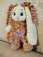 Вязаная плюшевая зайка в ярком платье Представляем очаровательную зайку, выполненную вручную из мягкой плюшевой пряжи. Эта игрушка не только подарит радость ребёнку, но и станет стильным элементом декора в детской комнате. Особенности: Материал: высококачественная плюшевая пряжа, приятная на ощупь, гипоаллергенная. Дизайн: длинные, объёмные ушки , украшенные разноцветными завитками, что придаёт игрушке индивидуальность; выразительные чёрные глазки с длинными ресничками, создающие «живой» взгляд; нежный розовый носик; лапки и туловище с объёмной текстурой. Одежда и аксессуары: яркое вязаное платье с разноцветным узором (сочетание жёлтых, розовых, голубых и оранжевых оттенков); платье украшено декоративными пуговицами в форме сердечек; вязаные пинетки в тон платью — добавляют образу завершённости и уюта.Бантики-завитушки на ушах,в тон платья. Размер: 32сантиметра (уточняйте при заказе). Удобно держать в руках, идеально для игр и обнимашек. Наполнитель: безопасный синтепух, обеспечивающий мягкость и упругость. Безопасность: все элементы надёжно закреплены, изделие абсолютно безопасно для детей. Преимущества:Ручная работа: каждая зайка уникальна, с небольшими отличиями в деталях вязки. Экологичные материалы: не вызывают аллергии, подходят даже для самых маленьких. Долговечность: пряжа устойчива к износу, игрушка сохраняет форму и цвет долгое время. Универсальность: подойдёт как для игр, так и для коллекционирования, украшения детской комнаты. Яркий дизайн: поднимет настроение и станет любимым другом ребёнка. Рекомендации по уходу:бережная ручная стирка в прохладной воде(30°);избегать использования агрессивных моющих средств;сушить в расправленном виде вдали от прямых солнечных лучей. Эта плюшевая зайка подарит тепло и уют, станет верным другом для вашего ребёнка или оригинальным подарком для близких. Подарите радость с этой очаровательной игрушкой!