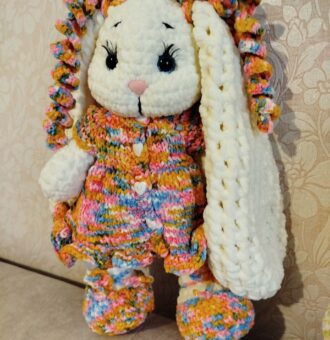 Вязаная плюшевая зайка в ярком платье Представляем очаровательную зайку, выполненную вручную из мягкой плюшевой пряжи. Эта игрушка не только подарит радость ребёнку, но и станет стильным элементом декора в детской комнате. Особенности: Материал: высококачественная плюшевая пряжа, приятная на ощупь, гипоаллергенная. Дизайн: длинные, объёмные ушки , украшенные разноцветными завитками, что придаёт игрушке индивидуальность; выразительные чёрные глазки с длинными ресничками, создающие «живой» взгляд; нежный розовый носик; лапки и туловище с объёмной текстурой. Одежда и аксессуары: яркое вязаное платье с разноцветным узором (сочетание жёлтых, розовых, голубых и оранжевых оттенков); платье украшено декоративными пуговицами в форме сердечек; вязаные пинетки в тон платью — добавляют образу завершённости и уюта.Бантики-завитушки на ушах,в тон платья. Размер: 32сантиметра (уточняйте при заказе). Удобно держать в руках, идеально для игр и обнимашек. Наполнитель: безопасный синтепух, обеспечивающий мягкость и упругость. Безопасность: все элементы надёжно закреплены, изделие абсолютно безопасно для детей. Преимущества:Ручная работа: каждая зайка уникальна, с небольшими отличиями в деталях вязки. Экологичные материалы: не вызывают аллергии, подходят даже для самых маленьких. Долговечность: пряжа устойчива к износу, игрушка сохраняет форму и цвет долгое время. Универсальность: подойдёт как для игр, так и для коллекционирования, украшения детской комнаты. Яркий дизайн: поднимет настроение и станет любимым другом ребёнка. Рекомендации по уходу:бережная ручная стирка в прохладной воде(30°);избегать использования агрессивных моющих средств;сушить в расправленном виде вдали от прямых солнечных лучей. Эта плюшевая зайка подарит тепло и уют, станет верным другом для вашего ребёнка или оригинальным подарком для близких. Подарите радость с этой очаровательной игрушкой!