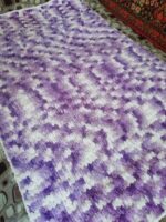 Этот плед выполнен из плюшевой пряжи Alize Puffy производства Турции , что придаёт ему особую мягкость и приятную текстуру. Изделие отличается объёмной вязкой с рельефным узором, создающим ощущение уюта и тепла. Особенности пледа: Цветовая гамма: сочетание нежных оттенков фиолетового и белого. Цвета плавно перетекают друг в друга, создавая эффект акварельного рисунка. Такой дизайн выглядит стильно и свежо, подойдёт для любого интерьера. Структура: вязка выполнена крупными петлями, что придаёт пледу дополнительную пушистость. Рельефный узор напоминает «петельчатую» технику, характерную для пряжи Puffy. Форма: прямоугольная, классическая форма пледа. Края аккуратно обработаны, без дополнительной каймы — акцент сделан на основной узор. Тактильные ощущения: благодаря плюшевой пряже плед очень мягкий, приятный на ощупь. Отлично подойдёт для использования в холодное время года — как для укрывания, так и в качестве декоративного элемента. Назначение: универсален — подойдёт для детской комнаты, спальни или гостиной. Можно использовать как покрывало, плед для отдыха или декоративный акцент на диване/кресле. Преимущества: гипоаллергенный материал (если пряжа акриловая); простота ухода (обычно такие пледы можно стирать в машинке на деликатном режиме); долговечность за счёт плотной вязки; эстетичный внешний вид — плед выглядит аккуратно и стильно. В целом, это уютный и практичный аксессуар, который добавит тепла и уюта в любой интерьер.