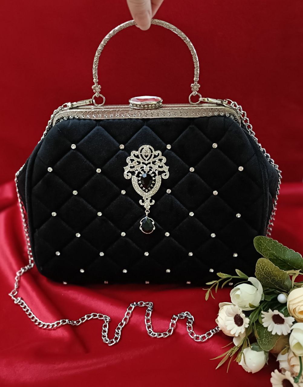 photo_2025-12-20_20-37-38 Представляю изысканную вечернюю сумочку "Версаль", воплощающую роскошь и утончённость. Выполненная из бархатистого чёрного велюра с изысканной стёжкой, она притягивает взгляды своим благородным блеском. Декоративные стразы, аккуратно инкрустированные на поверхности, добавляют нотку гламура, а витиеватый металлический декор с камнем в центре превращает аксессуар в настоящий шедевр. Элегантная ручка и цепочка позволяют носить сумочку как в руке, так и на плече — идеальный выбор для торжественного вечера.