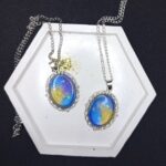 Кулоны «Звёздный шёпот» — эхо древних созвездий Перед вами не просто украшения, а магические реликвии, рождённые на стыке реальности и волшебства. Эти кулоны словно хранят в себе отблески далёких галактик, где звёзды сплетают свои истории в танце вечности. Каждый кулон обрамлён изящной металлической оправой в цвете серебра, напоминающей древние эльфийские узоры — будто искусные мастера зачаровали металл, чтобы он навеки хранил тайну небес. В центре — переливающийся состав, сотканный из оттенков ночного неба: глубокий синий плавно переходит в золотисто-жёлтый, словно рассвет, пробивающийся сквозь звёздную пыль. Маленькие искорки-звёзды, вкраплённые в состав, будто застыли в мгновении волшебства. Говорят, что каждая из них — это душа упавшей звезды, заключённая в амулет для защиты владельца. Эти звёзды шепчут древние заклинания, оберегая от бед и наполняя сердце вдохновением. Легенда гласит: тот, кто носит такой кулон, может услышать шёпот созвездий в тишине ночи. Они расскажут о забытых мирах, древних пророчествах и тайных тропах между измерениями. А если загадать желание под полной луной, держа кулон в ладони, оно непременно сбудется — ведь магия звёзд не знает преград. Позвольте этим кулонам стать вашими верными спутниками в путешествии по миру грёз и приключений. Они не просто украсят ваш образ — они станут частью вашей истории, наполняя каждый день магией и загадкой.