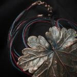Изысканное колье, центральным элементом которого служит лист садовой герани, выполненный с помощью техники гальванопластика. Лист, окрашенный в нежные оттенки оливкового и болотно-бирюзового, словно парит в воздухе — вощёный шнур искусно выходит из его боковинок, создавая иллюзию невесомости и лёгкого парения.