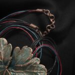 Изысканное колье, центральным элементом которого служит лист садовой герани, выполненный с помощью техники гальванопластика. Лист, окрашенный в нежные оттенки оливкового и болотно-бирюзового, словно парит в воздухе — вощёный шнур искусно выходит из его боковинок, создавая иллюзию невесомости и лёгкого парения.