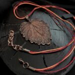 Изысканное колье, центральным элементом которого служит лист яснотки, виртуозно воссозданный в технике гальванопластика. Поверхность листа играет оттенками коричневого, медного и тёмно-шоколадного, создавая ощущение глубины и природной теплоты.