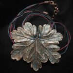 Изысканное колье, центральным элементом которого служит лист садовой герани, выполненный с помощью техники гальванопластика. Лист, окрашенный в нежные оттенки оливкового и болотно-бирюзового, словно парит в воздухе — вощёный шнур искусно выходит из его боковинок, создавая иллюзию невесомости и лёгкого парения.