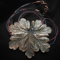 Изысканное колье, центральным элементом которого служит лист садовой герани, выполненный с помощью техники гальванопластика. Лист, окрашенный в нежные оттенки оливкового и болотно-бирюзового, словно парит в воздухе — вощёный шнур искусно выходит из его боковинок, создавая иллюзию невесомости и лёгкого парения.