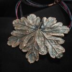 Изысканное колье, центральным элементом которого служит лист садовой герани, выполненный с помощью техники гальванопластика. Лист, окрашенный в нежные оттенки оливкового и болотно-бирюзового, словно парит в воздухе — вощёный шнур искусно выходит из его боковинок, создавая иллюзию невесомости и лёгкого парения.