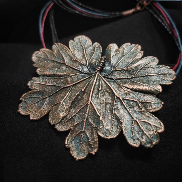 Изысканное колье, центральным элементом которого служит лист садовой герани, выполненный с помощью техники гальванопластика. Лист, окрашенный в нежные оттенки оливкового и болотно-бирюзового, словно парит в воздухе — вощёный шнур искусно выходит из его боковинок, создавая иллюзию невесомости и лёгкого парения.