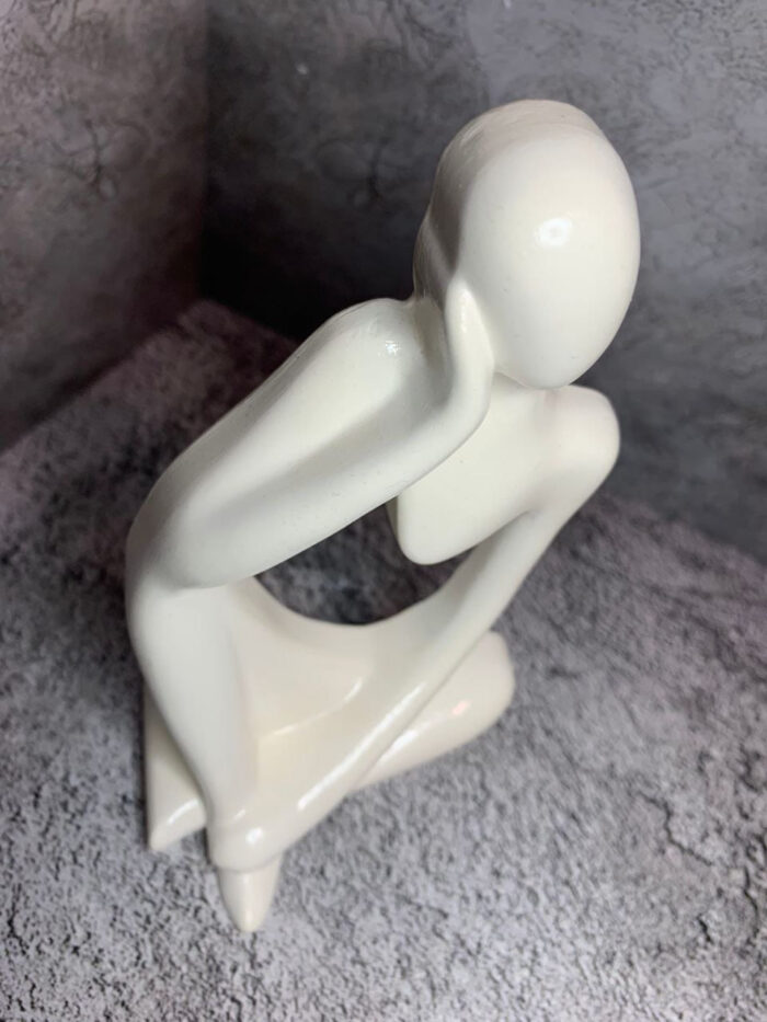 Элегантная интерьерная статуэтка, выполненная в абстрактном стиле, воплощает образ задумчивого человека, погружённого в размышления. Фигура сидит в расслабленной позе: одна рука поддерживает голову, другая естественно опущена, что создаёт ощущение глубокой задумчивости и внутреннего диалога.