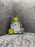 Представляем очаровательный брелок, выполненный в технике вышивки крестиком на пластиковой канве. Центральным элементом дизайна стал милый котик с расслабленным выражением мордочки, украшенный тремя ярко-жёлтыми цыплятами — один на голове и по одному с каждой стороны. Этот аксессуар сочетает в себе игривость и уют, станет стильным дополнением к ключам, рюкзаку или сумке.