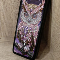 Элегантный футляр для очков, украшенный изысканной алмазной вышивкой с изображением совы, станет не только практичным аксессуаром, но и стильным элементом вашего образа. Центральным элементом дизайна является детализированное изображение совы, выполненное с использованием разноцветных страз и бусин — от нежно-розовых и перламутровых до насыщенных фиолетовых и золотистых оттенков.