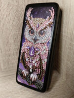 Элегантный футляр для очков, украшенный изысканной алмазной вышивкой с изображением совы, станет не только практичным аксессуаром, но и стильным элементом вашего образа. Центральным элементом дизайна является детализированное изображение совы, выполненное с использованием разноцветных страз и бусин — от нежно-розовых и перламутровых до насыщенных фиолетовых и золотистых оттенков.