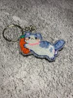 Представляем очаровательный брелок, выполненный в технике вышивки крестиком на пластиковой канве. Центральным элементом дизайна стал милый котик, который держит в лапках ярко-оранжевую морковку с зелёной ботвой. Этот аксессуар сочетает в себе игривость и утончённость, станет стильным дополнением к ключам, рюкзаку или сумке