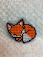 Представляем очаровательную брошь в виде спящей лисы, выполненную в стиле пиксель-арт — милый и стильный аксессуар для любителей животных и ретро-игр!