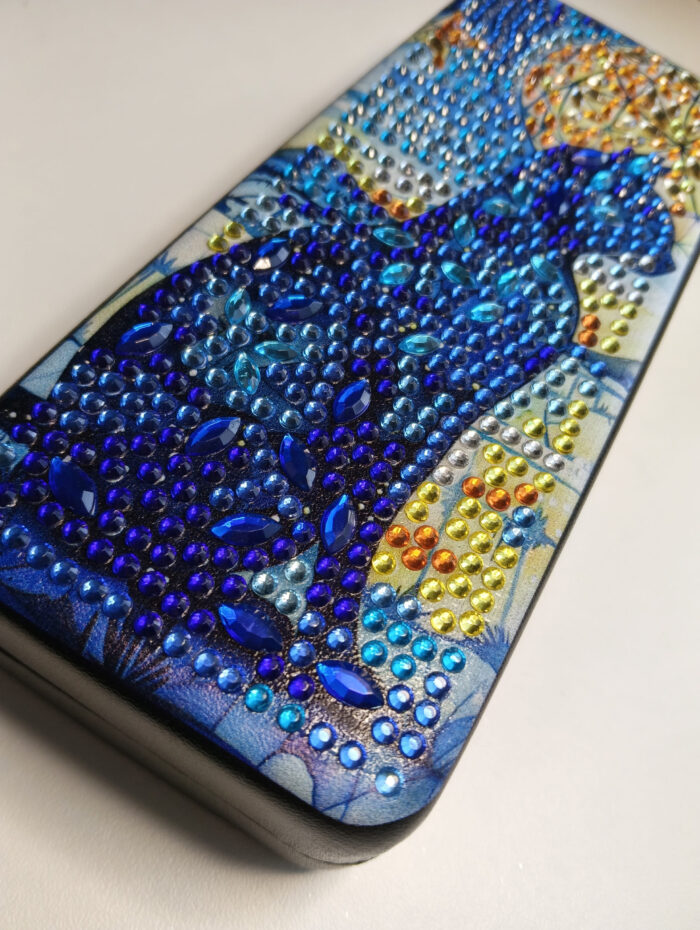 Роскошный футляр для очков, украшенный авторской алмазной вышивкой, превратит хранение аксессуаров в настоящее эстетическое удовольствие. Центральным элементом дизайна стал загадочный силуэт кошки, выполненный с использованием страз насыщенных синих, фиолетовых и бирюзовых оттенков.
