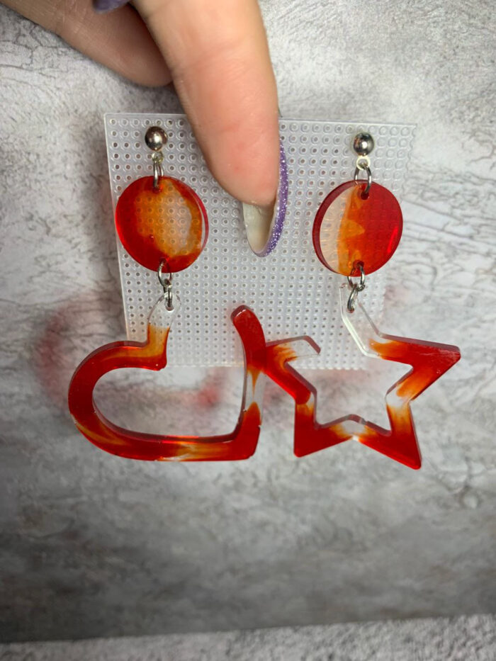 Представляем эффектные серьги из эпоксидной смолы, которые станут ярким акцентом в любом образе! Эта пара сочетает в себе два выразительных элемента: округлый диск и крупную геометрическую фигуру — сердце и звезду. Насыщенная красно-оранжевая гамма с полупрозрачными переливами создаёт ощущение огненного закатного неба, а плавные переходы оттенков придают украшению глубину и объём.