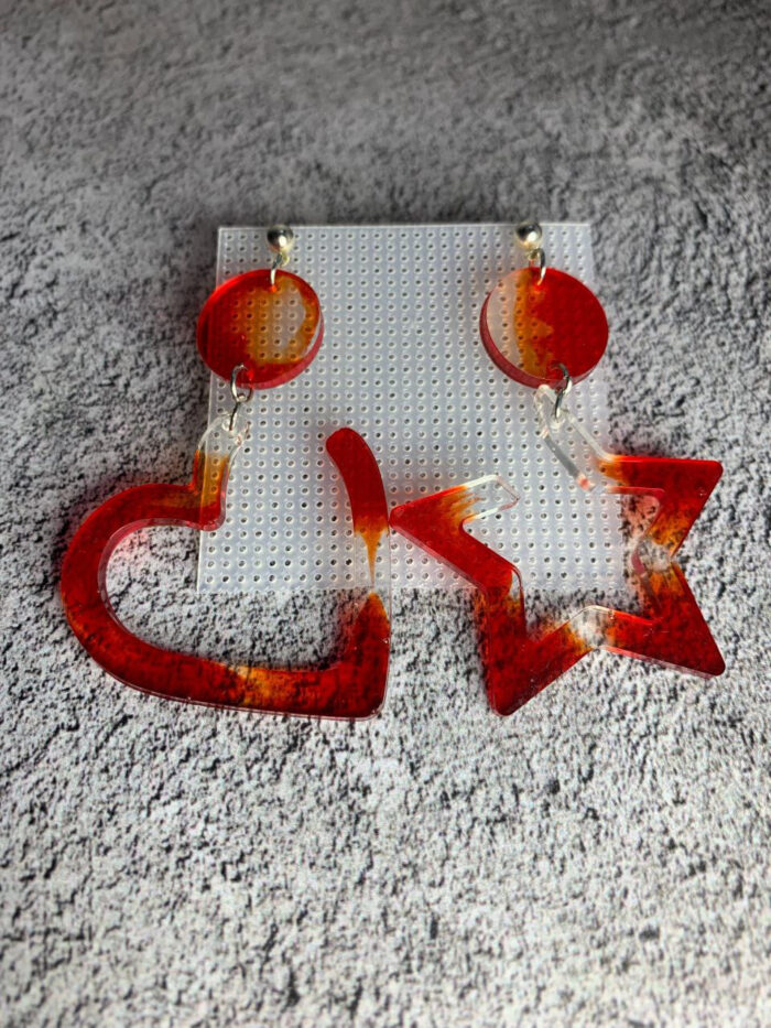 Представляем эффектные серьги из эпоксидной смолы, которые станут ярким акцентом в любом образе! Эта пара сочетает в себе два выразительных элемента: округлый диск и крупную геометрическую фигуру — сердце и звезду. Насыщенная красно-оранжевая гамма с полупрозрачными переливами создаёт ощущение огненного закатного неба, а плавные переходы оттенков придают украшению глубину и объём.