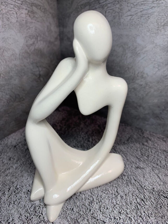 Элегантная интерьерная статуэтка, выполненная в абстрактном стиле, воплощает образ задумчивого человека, погружённого в размышления. Фигура сидит в расслабленной позе: одна рука поддерживает голову, другая естественно опущена, что создаёт ощущение глубокой задумчивости и внутреннего диалога.