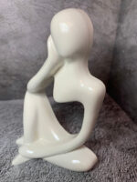 Элегантная интерьерная статуэтка, выполненная в абстрактном стиле, воплощает образ задумчивого человека, погружённого в размышления. Фигура сидит в расслабленной позе: одна рука поддерживает голову, другая естественно опущена, что создаёт ощущение глубокой задумчивости и внутреннего диалога.