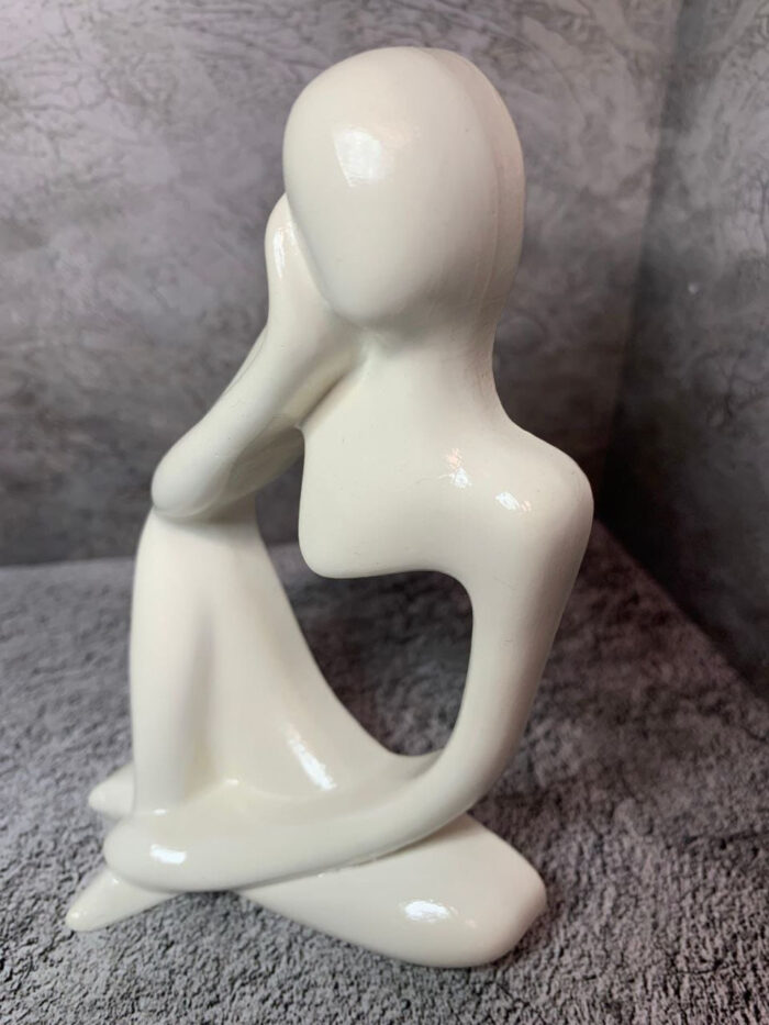 Элегантная интерьерная статуэтка, выполненная в абстрактном стиле, воплощает образ задумчивого человека, погружённого в размышления. Фигура сидит в расслабленной позе: одна рука поддерживает голову, другая естественно опущена, что создаёт ощущение глубокой задумчивости и внутреннего диалога.