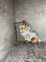 Представляем очаровательный брелок, выполненный в технике вышивки крестиком на пластиковой канве. Центральным элементом дизайна стал расслабленный котик в характерной «ленивой» позе — лежащий на боку с поднятой лапкой. Этот аксессуар сочетает в себе игривость и уют, станет стильным дополнением к ключам, рюкзаку или сумке.