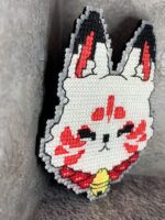 Представляем эксклюзивную брошь в виде головы кицуне (мифической лисы из японской мифологии), выполненную в технике вышивки крестиком на пластиковой канве. Этот аксессуар сочетает в себе элементы традиционного японского искусства и современный стиль ручной работы.