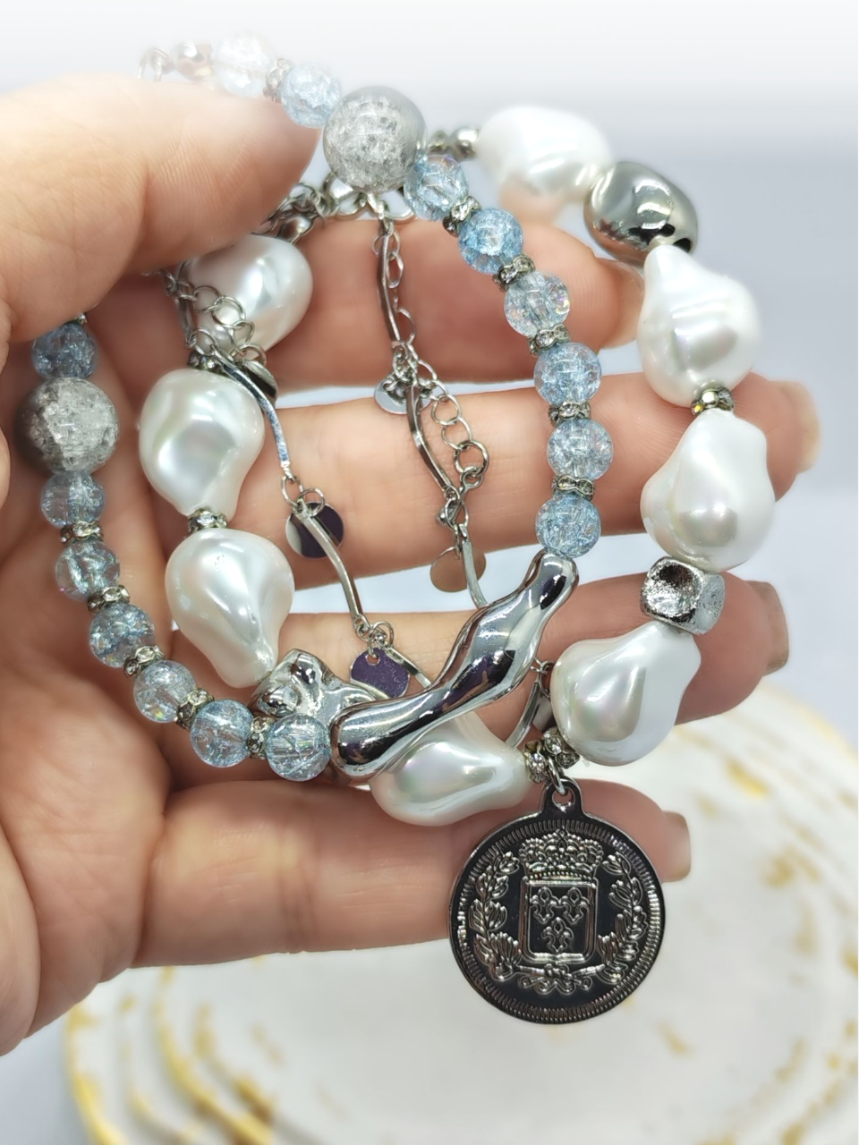 Браслет с жемчугом Майорка и сахарным кварцем: воплощение элегантности и индивидуальности Ищете украшение, которое подчеркнёт вашу утончённость и добавит нотку роскоши в любой образ? Представляем вам эксклюзивный браслет, сочетающий в себе изысканность жемчуга, нежность кварца и изящество серебряных элементов. Почему этот браслет заслуживает вашего внимания? · Роскошный дизайн. Крупные жемчужные бусины неправильной формы создают ощущение природной гармонии и уникальности. Нежно-голубой кварц напоминает о морском бризе и добавляет свежести образу. · Сочетание материалов. Серебряные элементы разной формы (гладкие, фактурные, изогнутые) создают интересную игру линий и текстур, делая браслет по-настоящему уникальным. · Особая деталь — монета-подвеска. Центральный элемент украшения — стилизованная монета с рельефным изображением. Она придаёт браслету винтажный шарм и делает его настоящим акцентом в образе. · Универсальность. Этот браслет легко сочетается как с повседневной одеждой, так и с вечерними нарядами. Он подойдёт для офиса, романтического ужина или торжественного мероприятия. · Три в одном. Этот аксессуар можно разделить на три самостоятельных браслета. Можно носить все сразу или по оному... Все, как пожелает ваше настроение · Качество исполнения. Каждый элемент тщательно подобран и надёжно закреплён. Браслет удобен в носке и не теряет внешний вид со временем. Идеальный подарок! Ищете подарок для особенной женщины? Этот браслет станет символом вашей заботы и внимания. Он подойдёт как для молодой девушки, так и для зрелой дамы, ценящей классику и элегантность. Не упустите возможность пополнить свою коллекцию украшений настоящим произведением искусства! Добавьте этот браслет в корзину уже сегодня и позвольте себе наслаждаться его красотой каждый день. Для заказа и по всем вопросам обращайтесь Телефон: +79817339605 WhatsApp: wa.me/79817339605 Группа в Telegram: t.me/LanaMir03 Сообщения группы VK: vk.me/lanamirc Группа VK, где вы найдете еще больше украшений: https://vk.com/lanamirc Или можно оформить заказ и задать вопрос прямо здесь, на нашем маркетплейсе https://marketcraft.ru/store/lanamir/ Нас находят по запросам: Браслет ручной работы, жемчуг, кварц, сахарный кварц, серебро, бусины, подвеска-монета, винтажный стиль, элегантность, украшение, женский аксессуар, ручная работа, изысканность, перламутр, голубые бусины, декоративные элементы, стильный браслет, ювелирное изделие, аксессуар для образа, дизайнерский браслет, браслет с камнями, тройной браслет